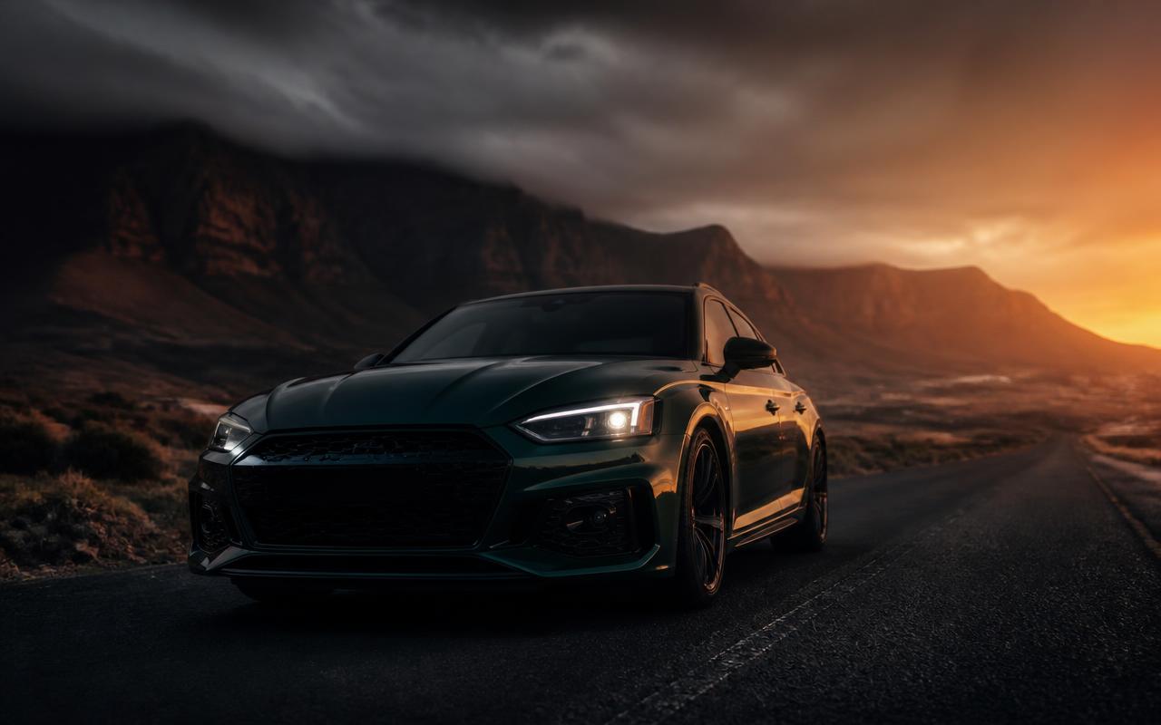 Dark modern car on an open road at dusk with mountains behind it